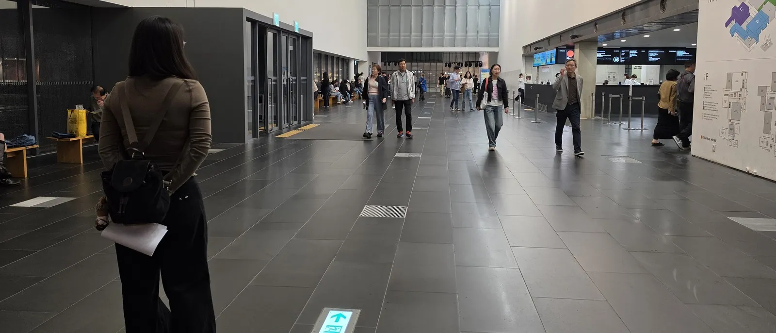 A Chainjee researcher, notes in hand, observing visitors in a museum lobby in Seoul